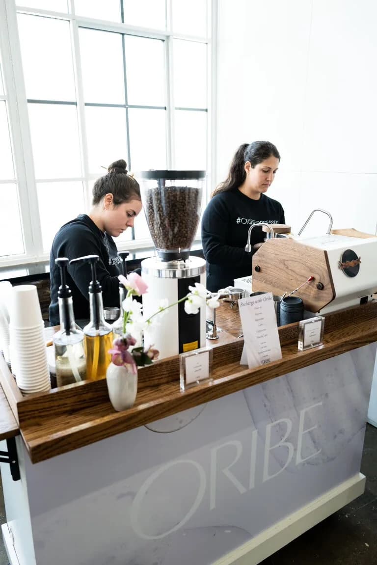 Two Anechó baristas working from a brand-wrapped coffee cart at a beauty brand launch event