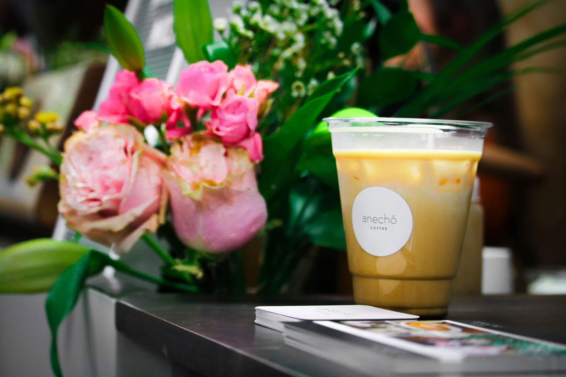 Iced latte in an Anechó branded cup beside fresh flowers at a corporate wellness event